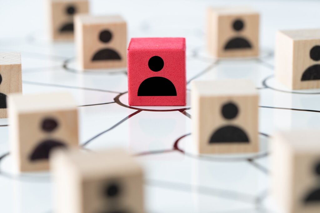 Red block representing a central figure in a network of wooden blocks with human icons, symbolizing social media management and audience engagement for brand growth.